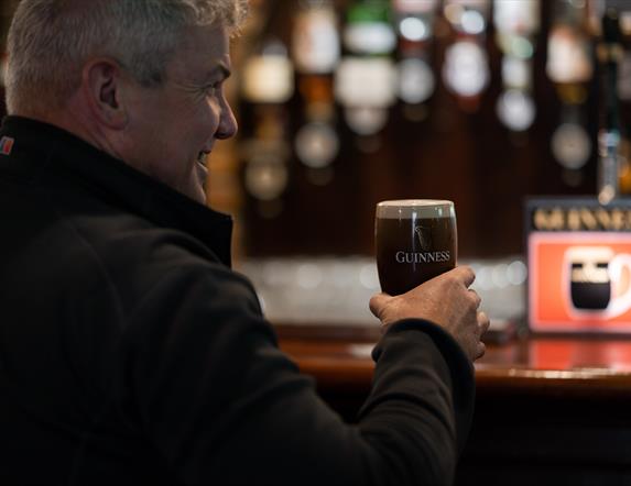 Gentleman drinking a freshly poured pint of Guinness in a branded glass at the bar of Charlie's Bar Enniskillen