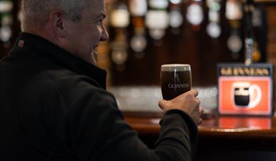 Gentleman drinking a freshly poured pint of Guinness in a branded glass at the bar of Charlie's Bar Enniskillen