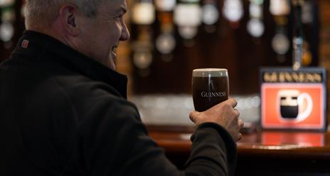 Gentleman drinking a freshly poured pint of Guinness in a branded glass at the bar of Charlie's Bar Enniskillen