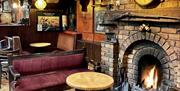 Cosy seating area beside an open fire with old Irish artefacts displayed on the mantle and surrounding walls at Charlie's Bar Enniskillen.
