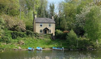 A house in a wooded area with a river and boats outside.